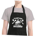 Black cooking apron with adjustable neck strap and humorous "well seasoned" design