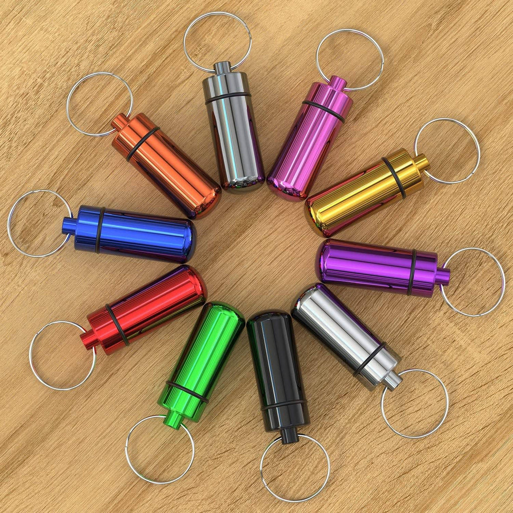 Assorted color pill cases with metal key rings laid out on wood surface.
