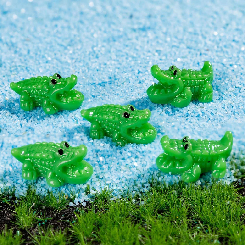 Assorted green mini crocodile resin figurines on blue gravel with grass nearby