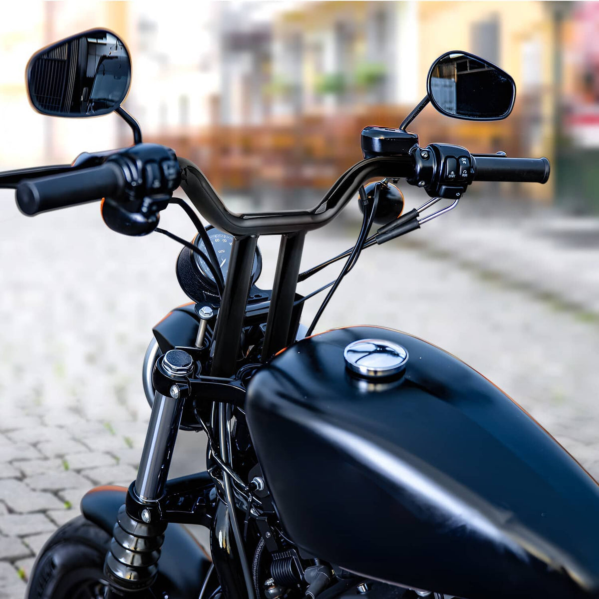 Black T-bar handlebar with high rise, grips, and controls on a dark motorcycle