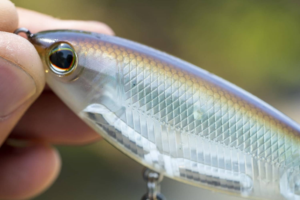 Close-up of a silver, scale-textured fishing lure with round painted eye