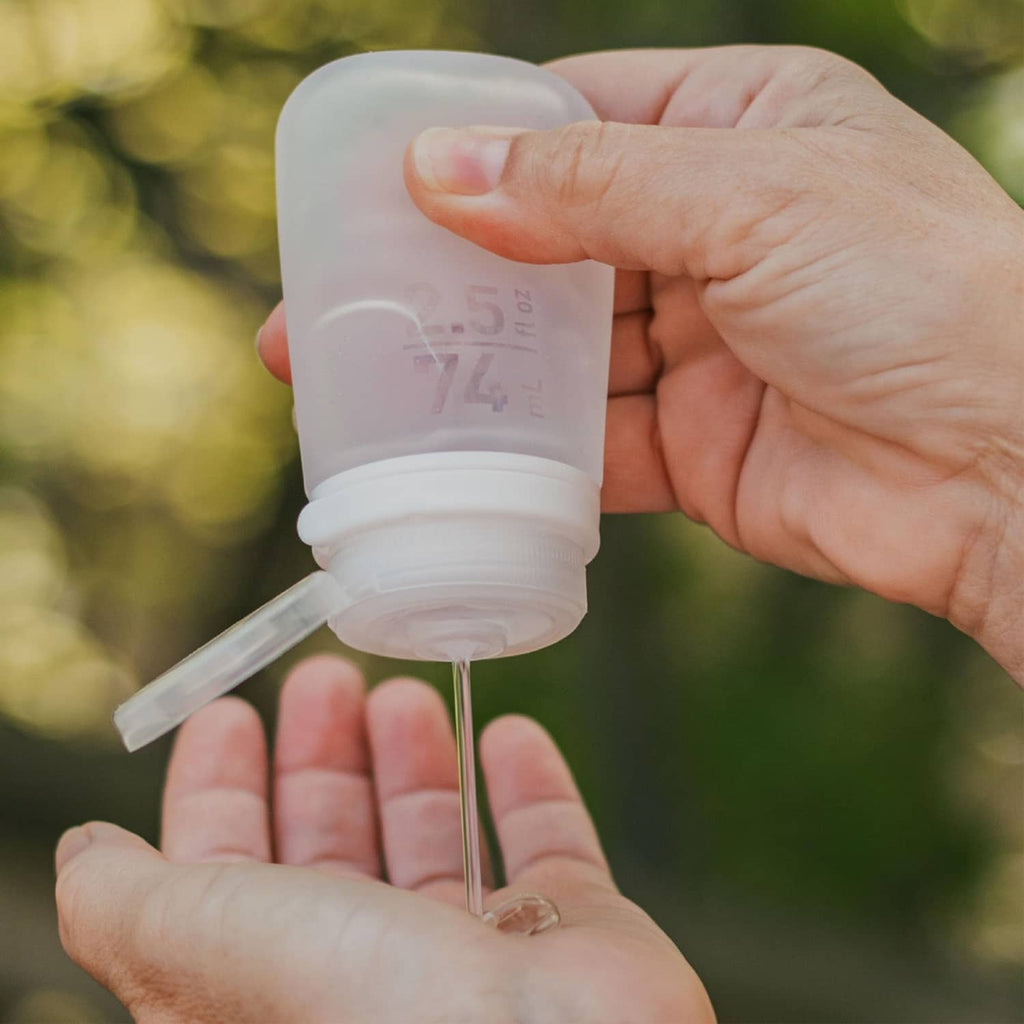 Silicone travel bottle being filled in hands, white bottle with pour spout