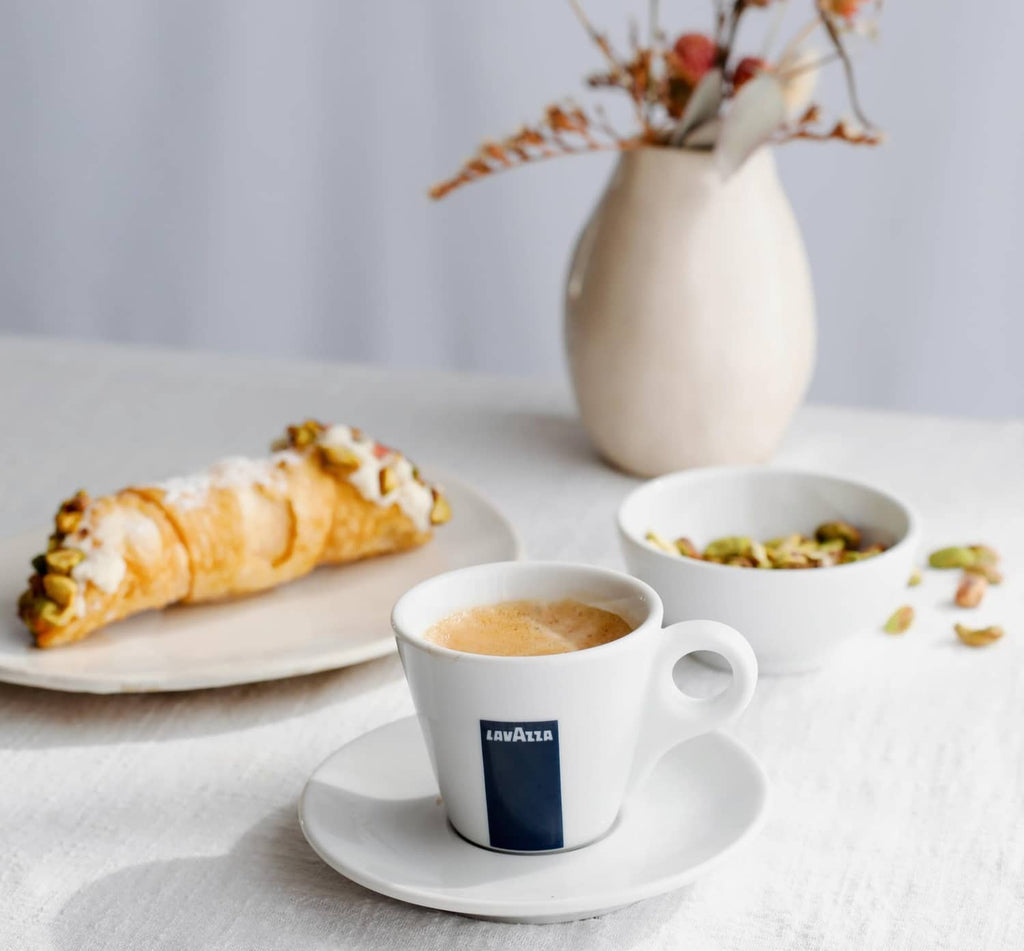 Lavazza coffee cup on saucer with pastries and a bowl of nuts on the table