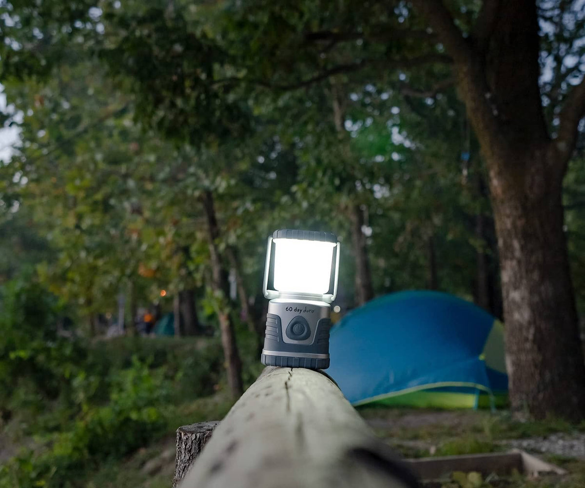 Portable LED lantern glowing outdoors, square white diffuser and gray ribbed housing