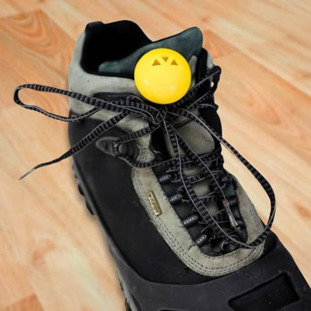Yellow 1-inch deodorizer sphere with star logo resting on black sneakers.