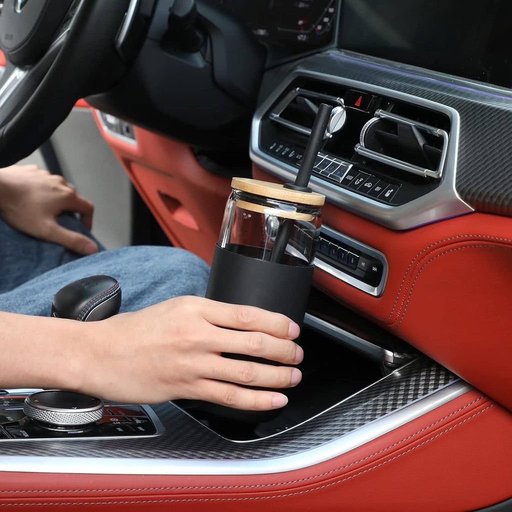 Black silicone-sleeved glass tumbler with straw in car cupholder