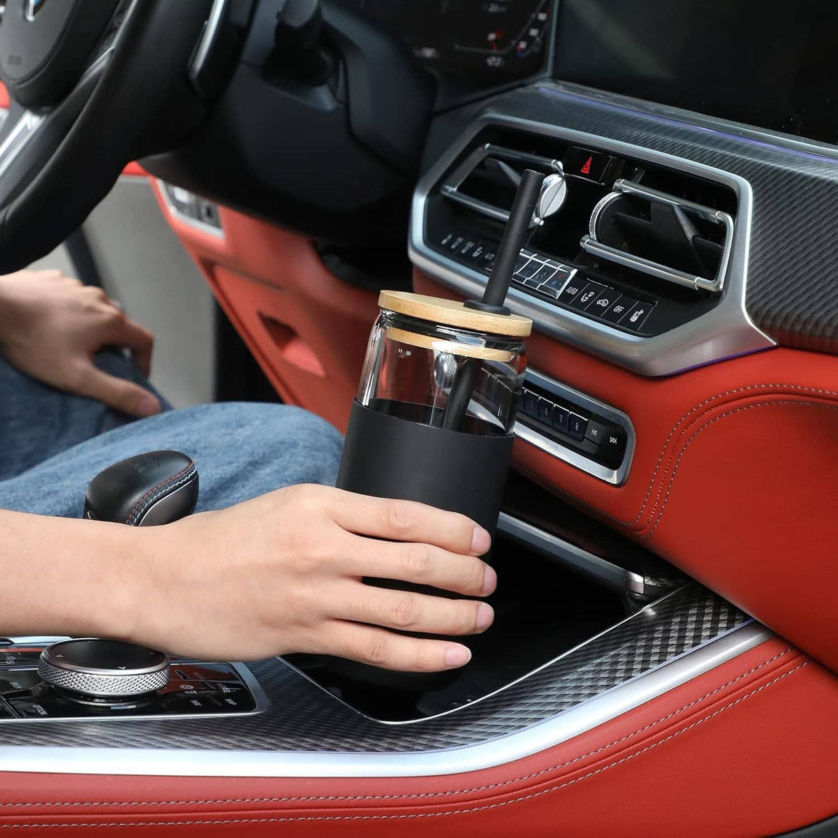Black silicone-sleeved glass tumbler with straw in car cupholder