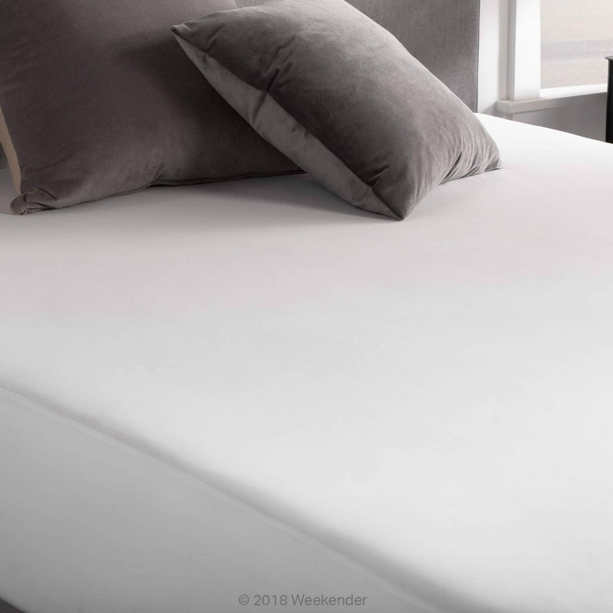 Fitted jersey mattress protector on bed with white cover and stitched gray trim