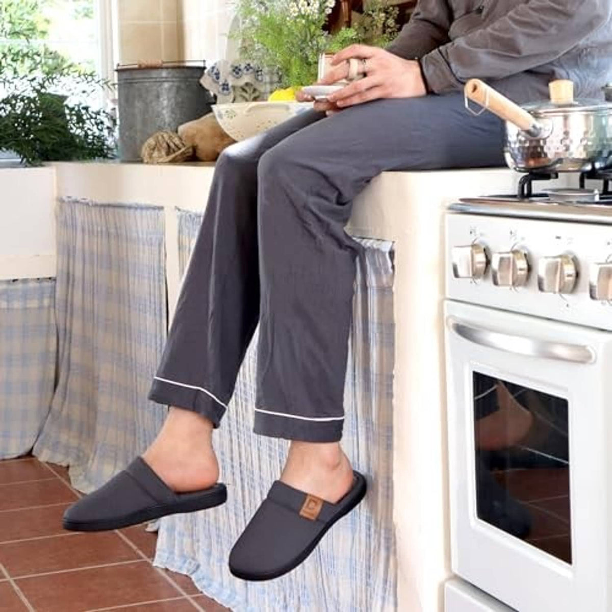 Men wearing dark gray slip-on slippers with cushioned plush lining in a kitchen setting