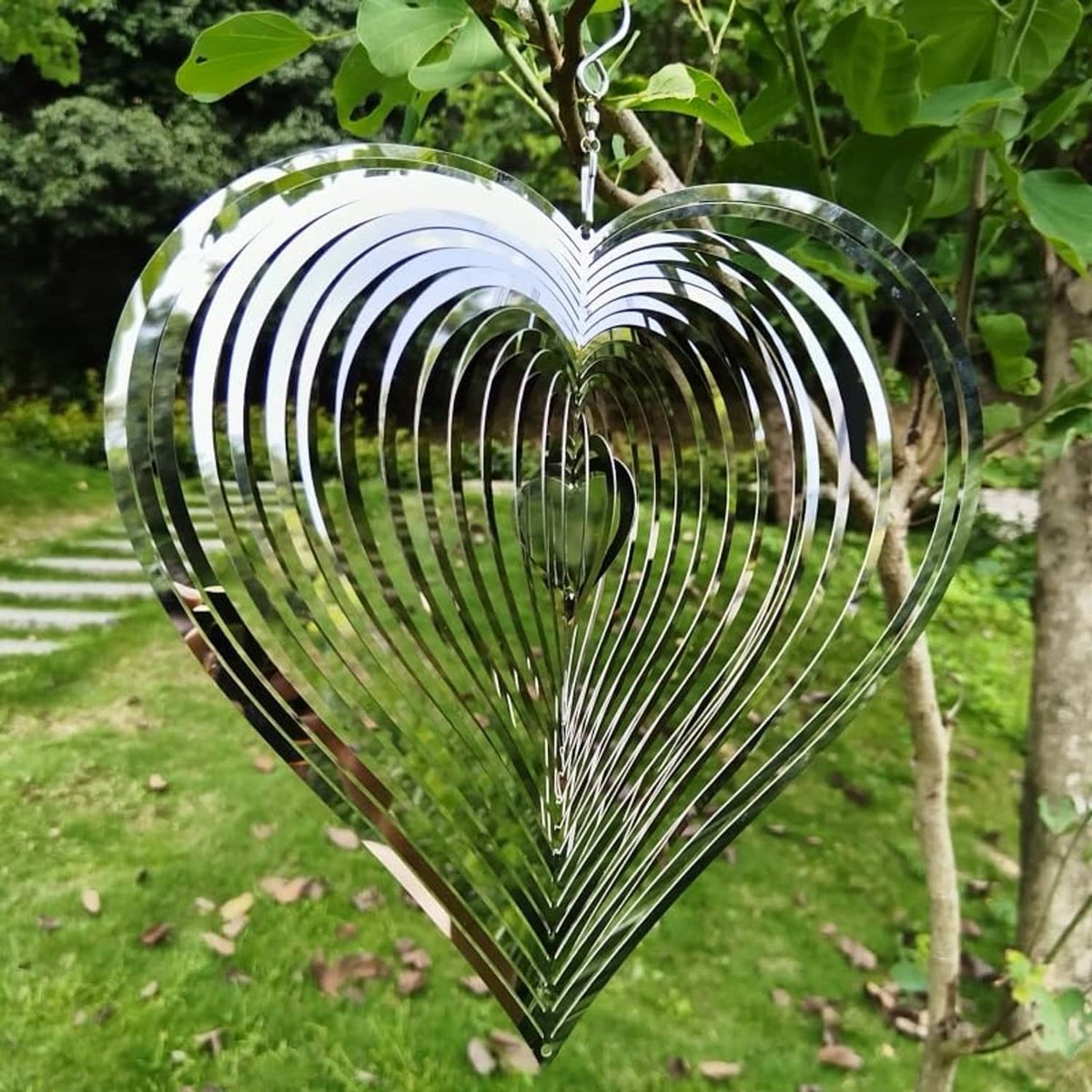 Heart garden wind chime spinner hanging on a branch, reflective silver spiral blades