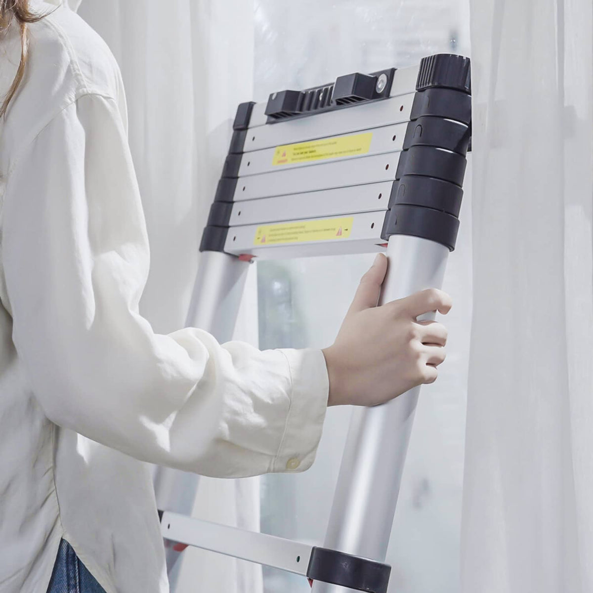 Aluminum telescoping ladder held by a user, with black top handle and white step panels