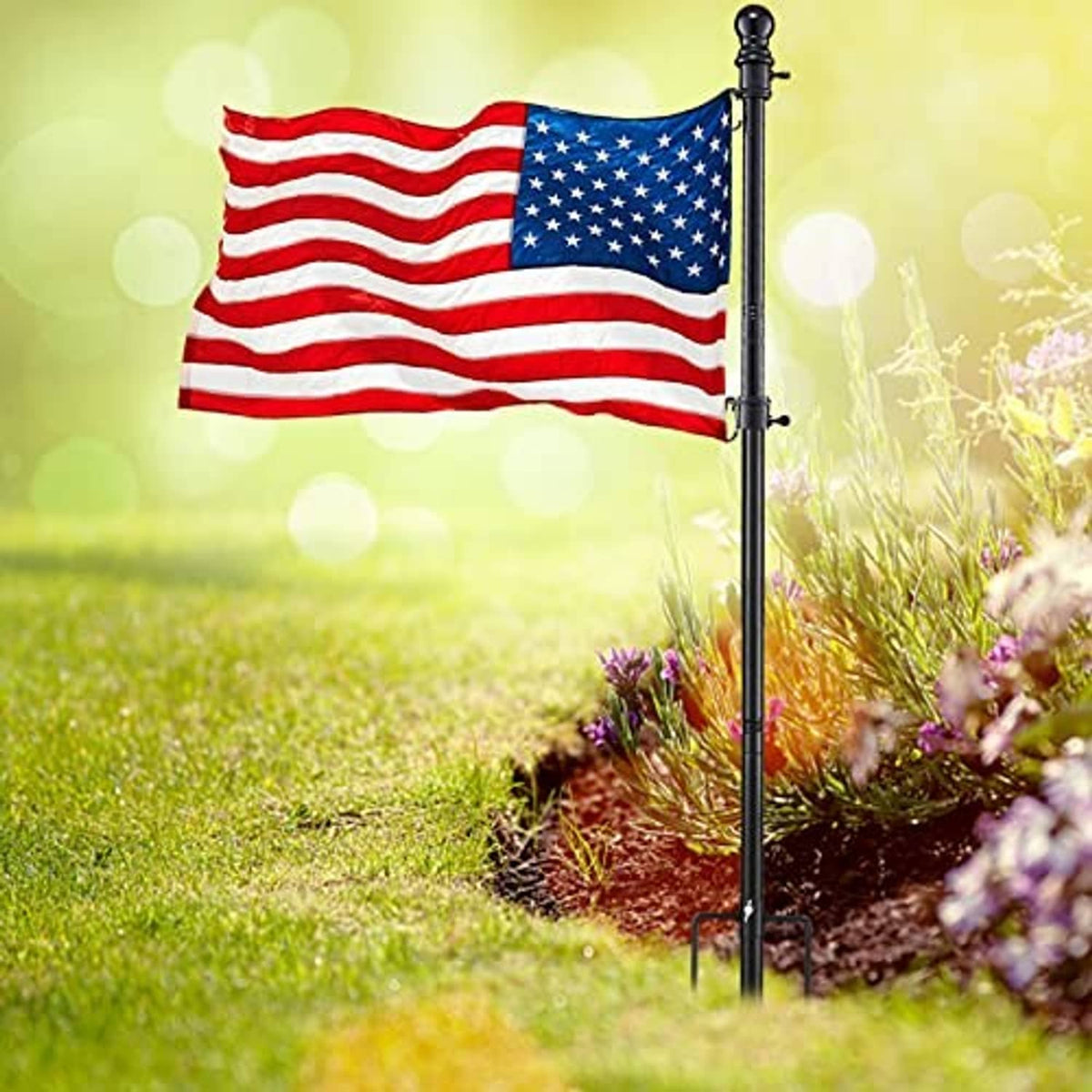 American flag waving on a black pole planted in the yard.