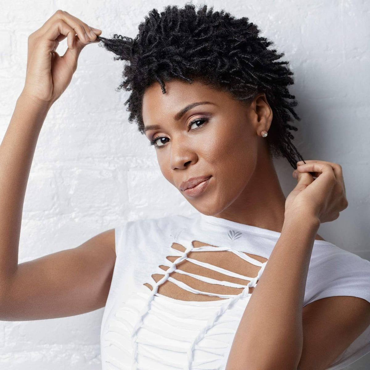 Woman with voluminous black curly hair, hands adjusting strands, white top