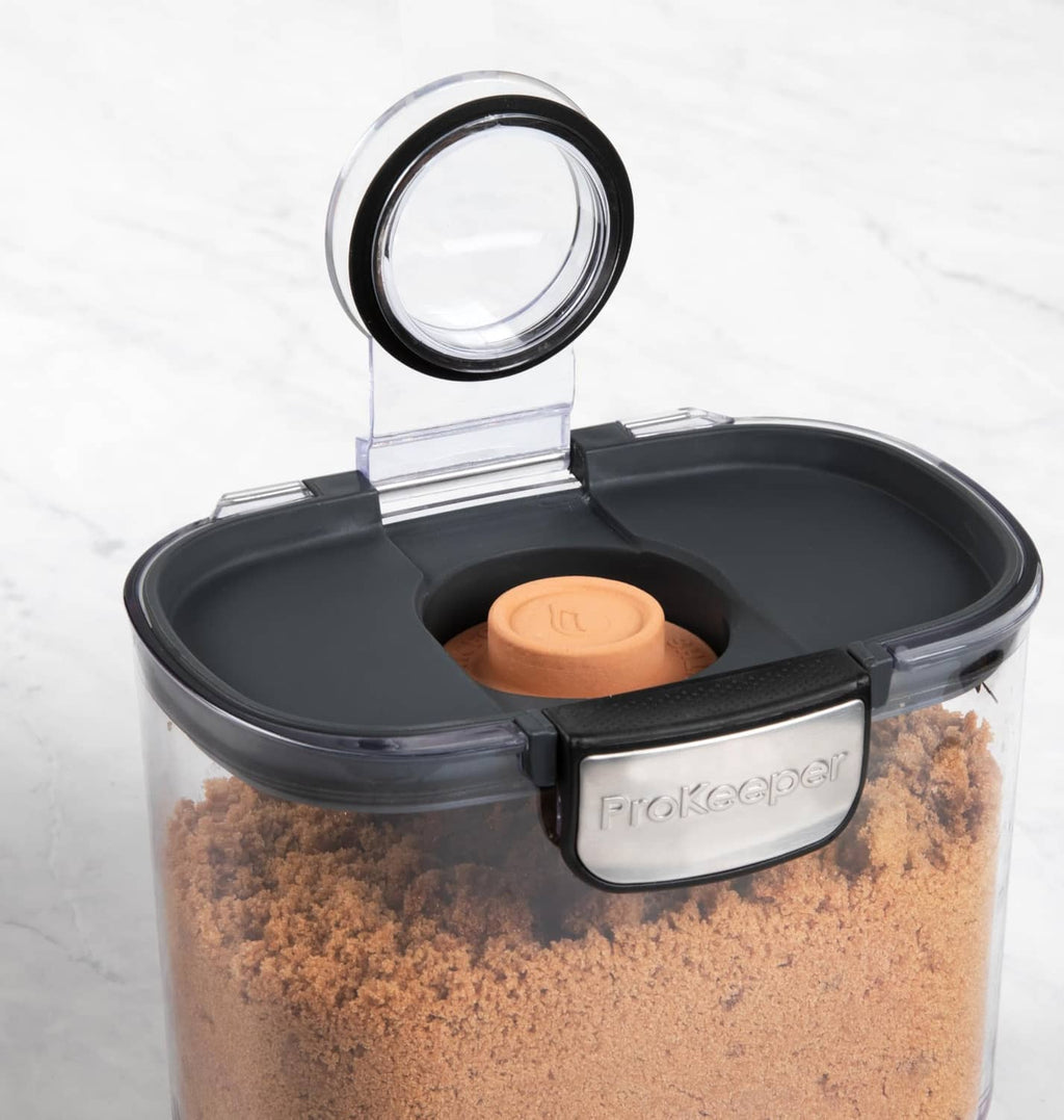 Clear airtight container with black lid, open top showing orange measuring cup and grains