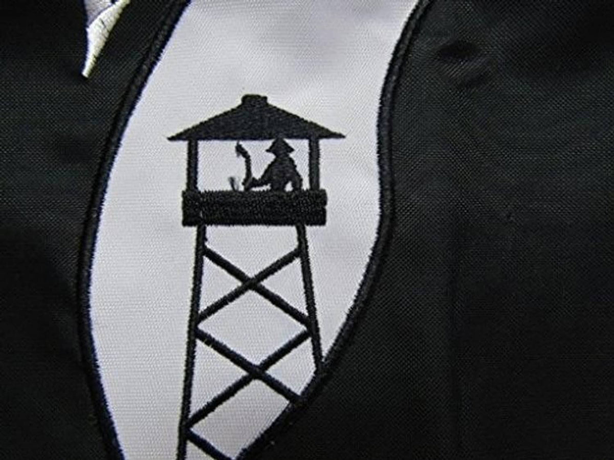 Close-up of embroidered POW*MIA banner emblem with white building icon on black
