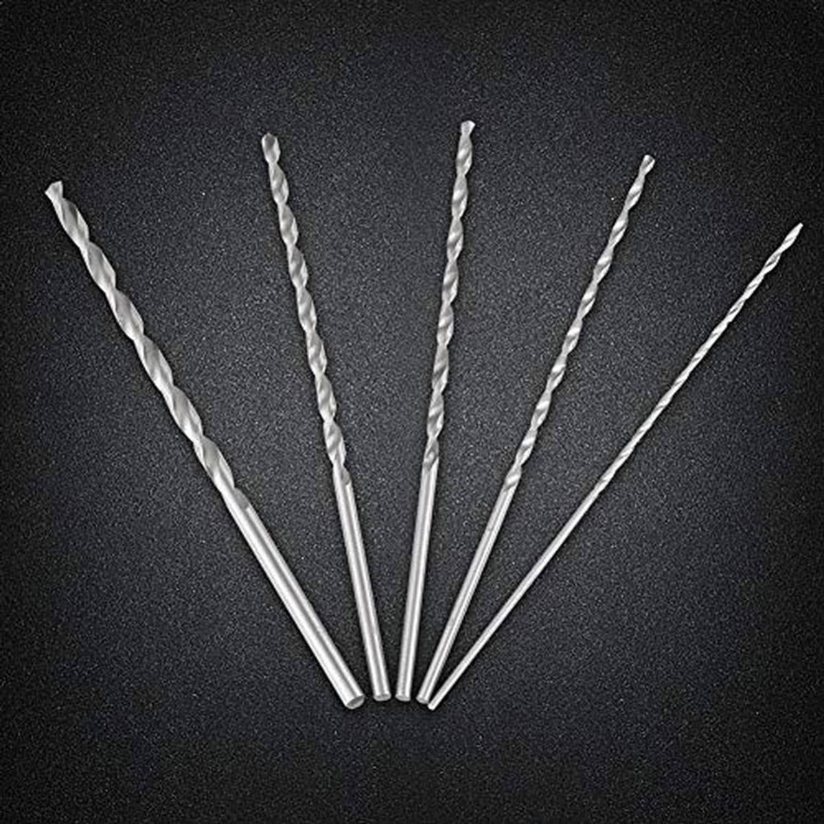 Five silver spiral twist drill bits fanned out on a dark surface