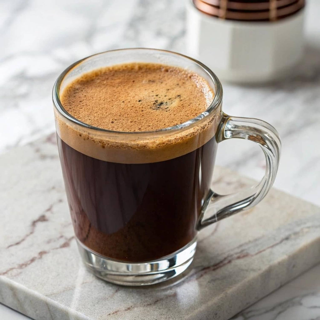 Glass mug filled with dark coffee, frothy crema on top