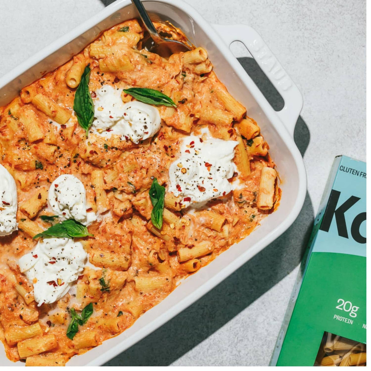 Baked ziti pasta in a white dish with melted cheese and basil leaves