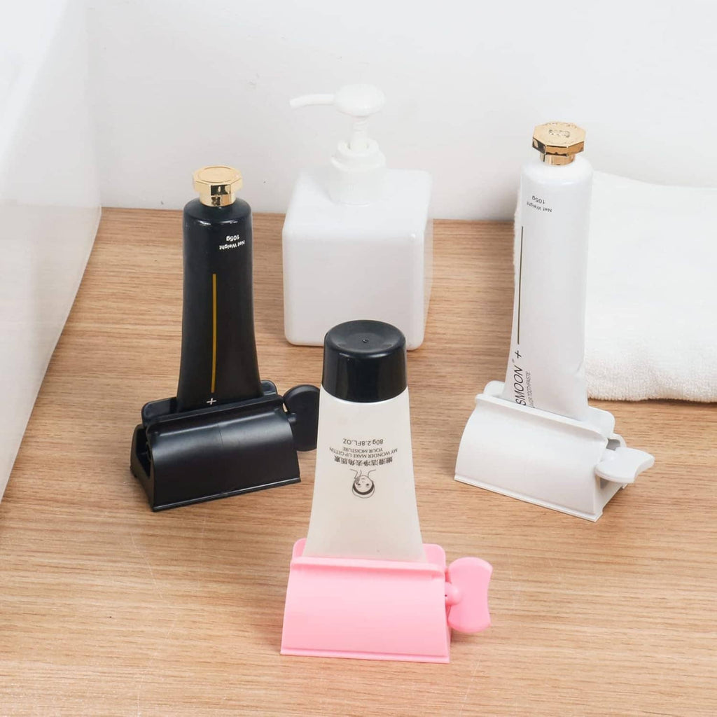 Toothpaste tube squeezer set on countertop: pink, white, black, and additional holders