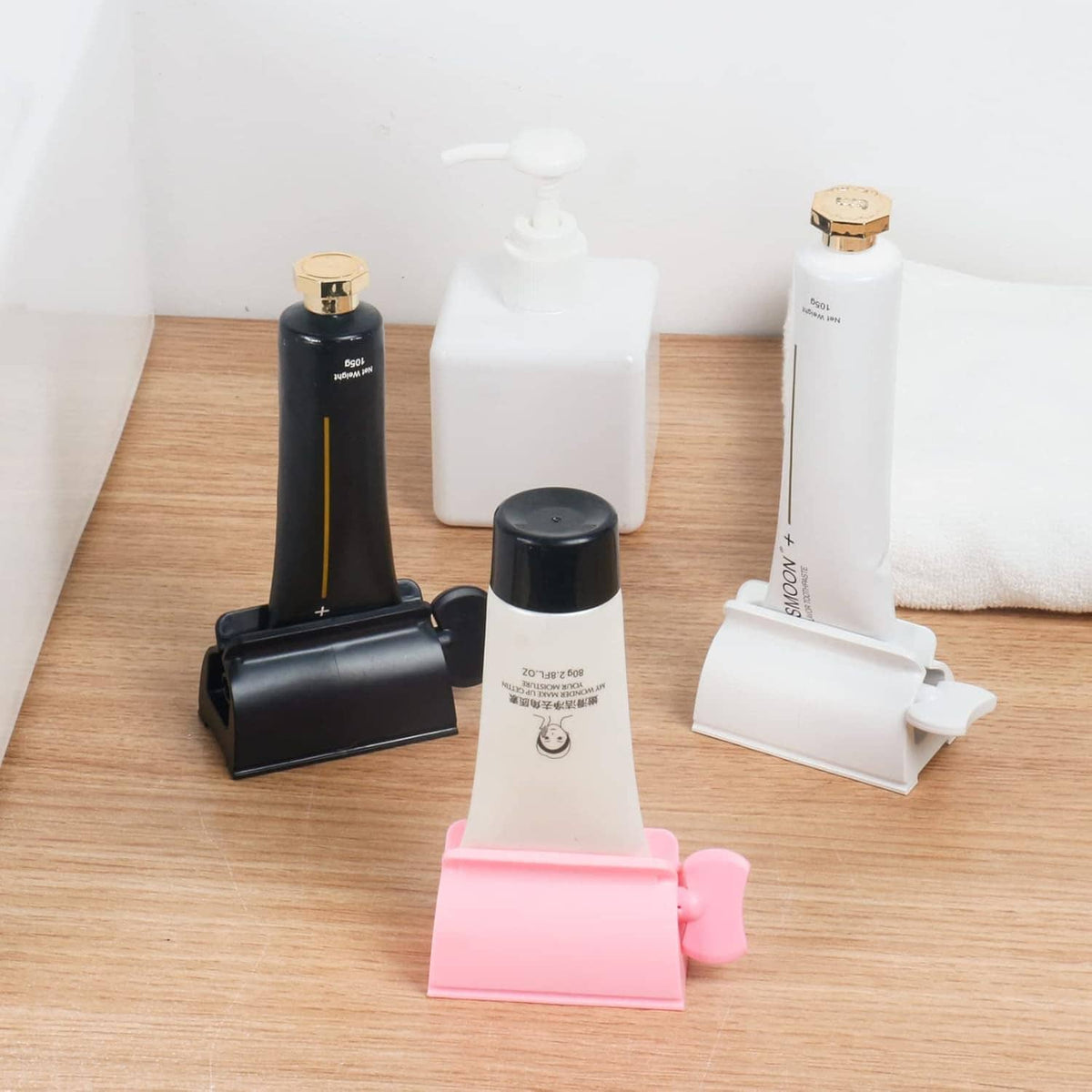 Toothpaste tube squeezer set on countertop: pink, white, black, and additional holders