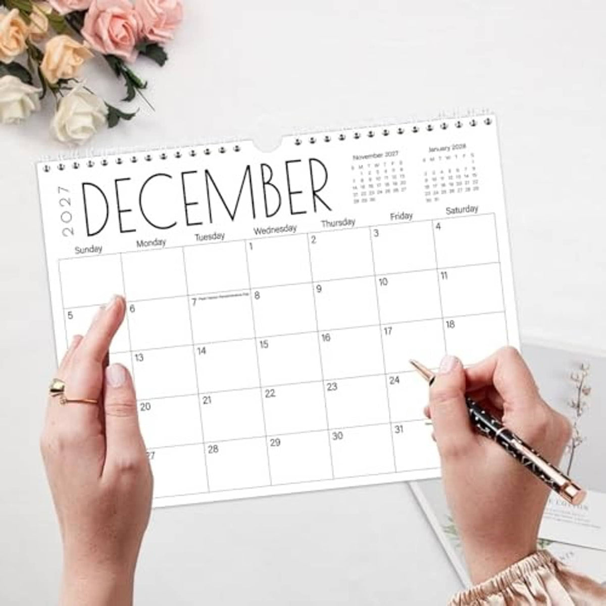 Wall calendar with spiral binding, December 2026 grid marked by hands