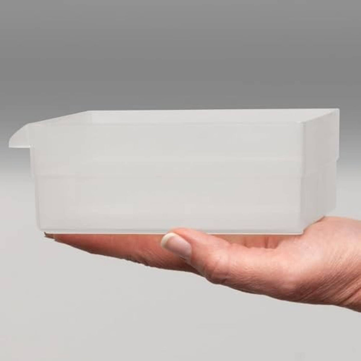 Hand holding a white plastic drawer insert or bin, side view
