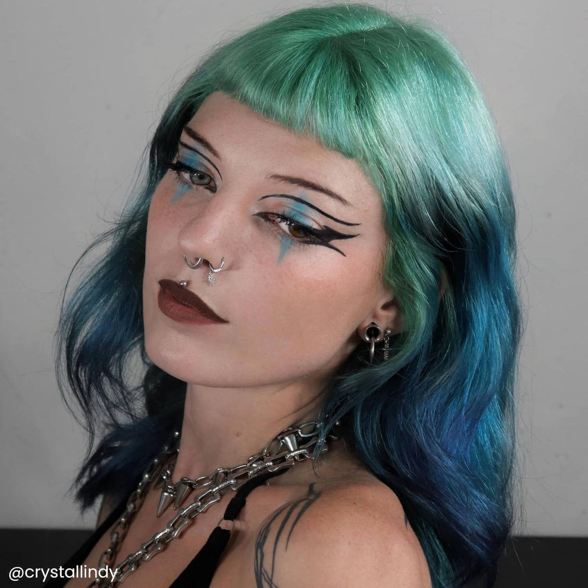 Short layered hair with teal-blue and green highlights, styled bob