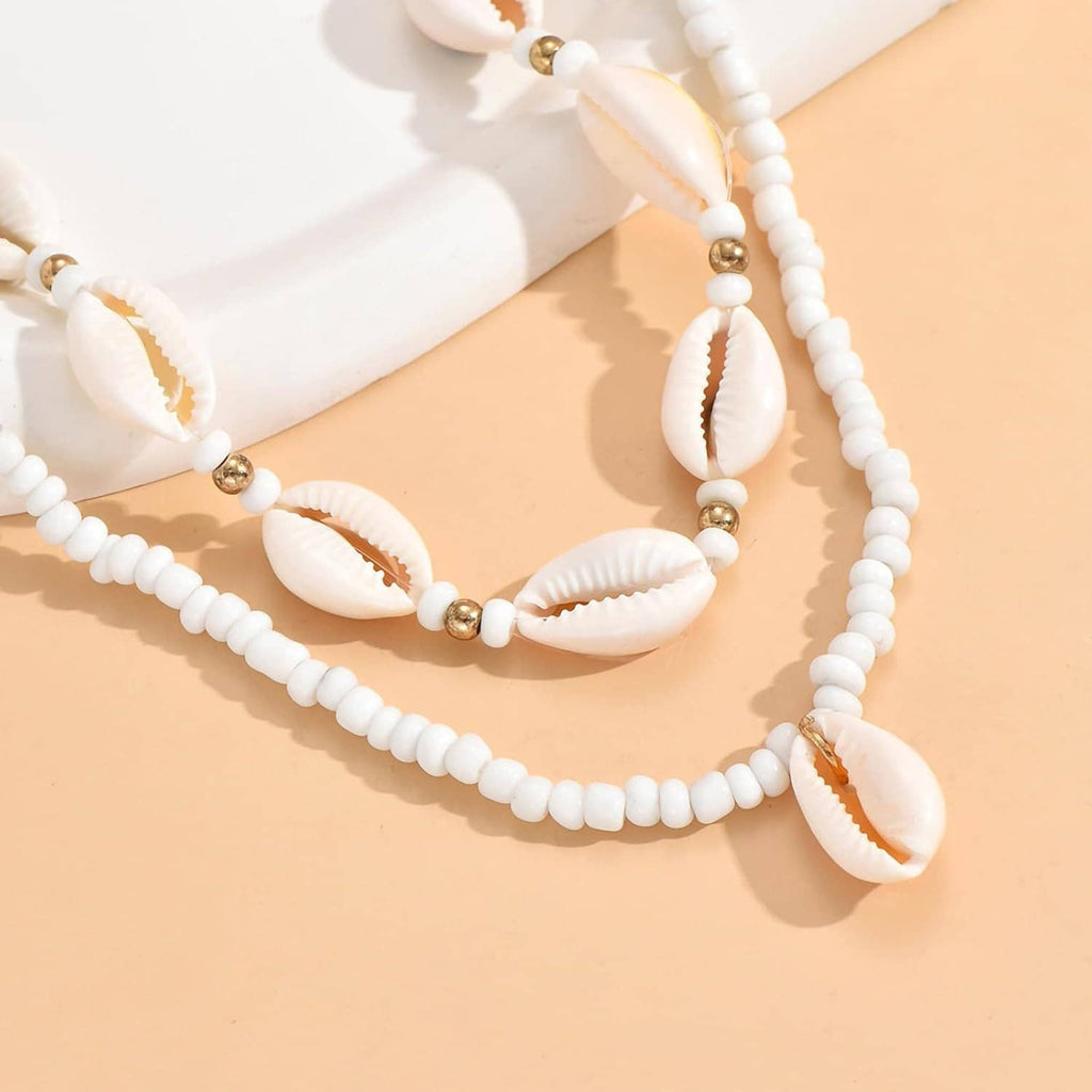 Beaded cowrie shell necklace with white beads, gold-tone spacers, and dangling shell