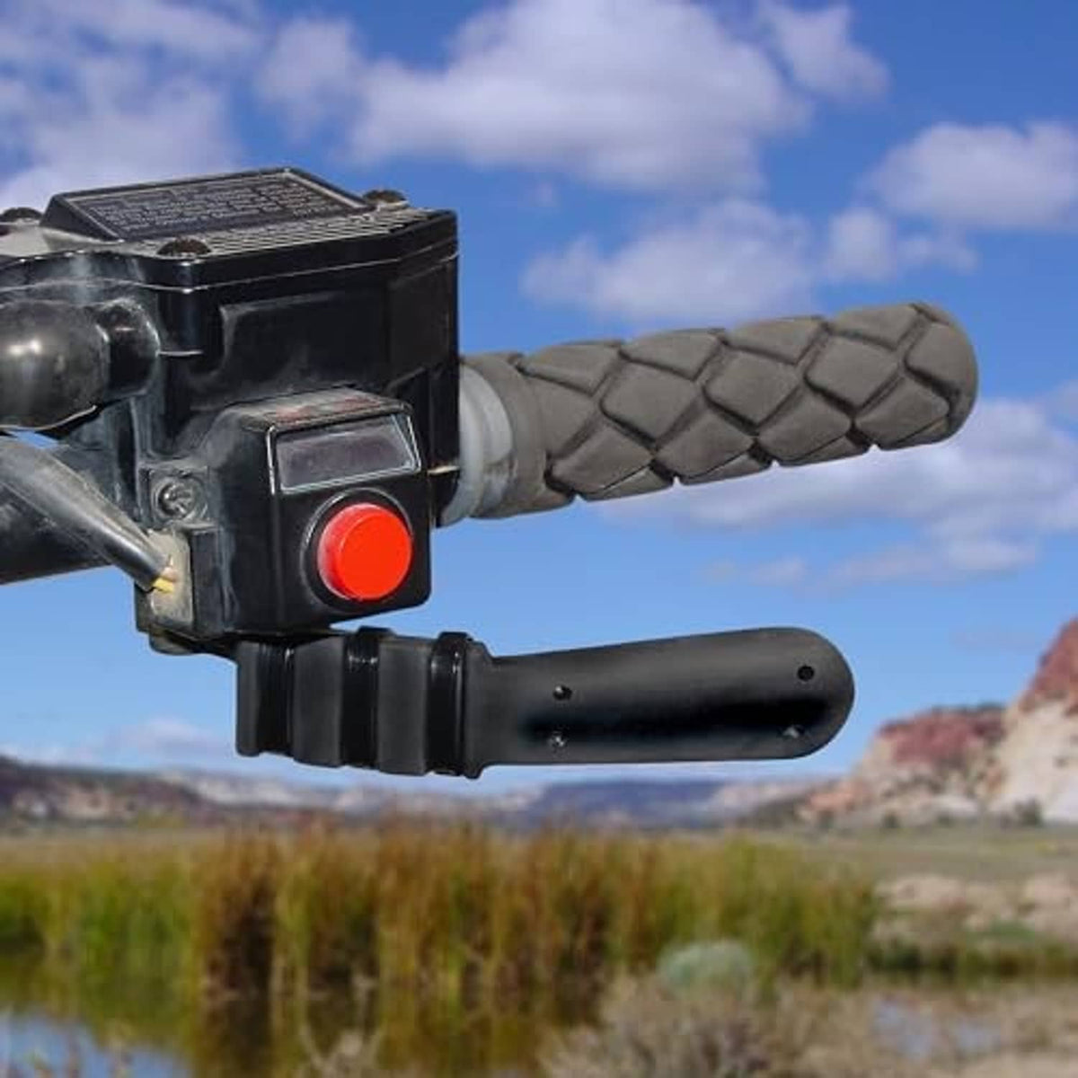 Throttle thumb extender on ATV control housing with red button and textured gray grip