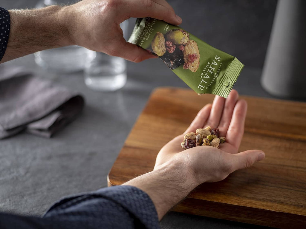 Hands pouring Sahale Snacks glazed nut mix from a green bag onto a wooden surface