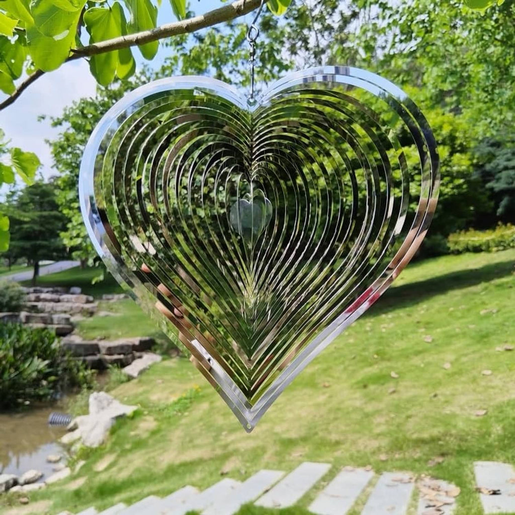 Heart wind spinner with reflective metal spirals suspended from an outdoor hook