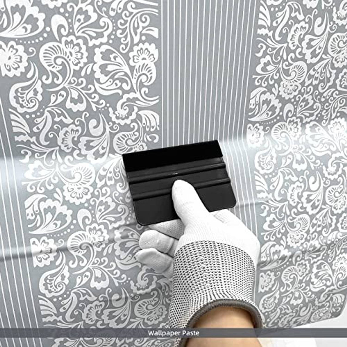 Black felt-edge squeegee smoothing wallpaper paste onto patterned wall