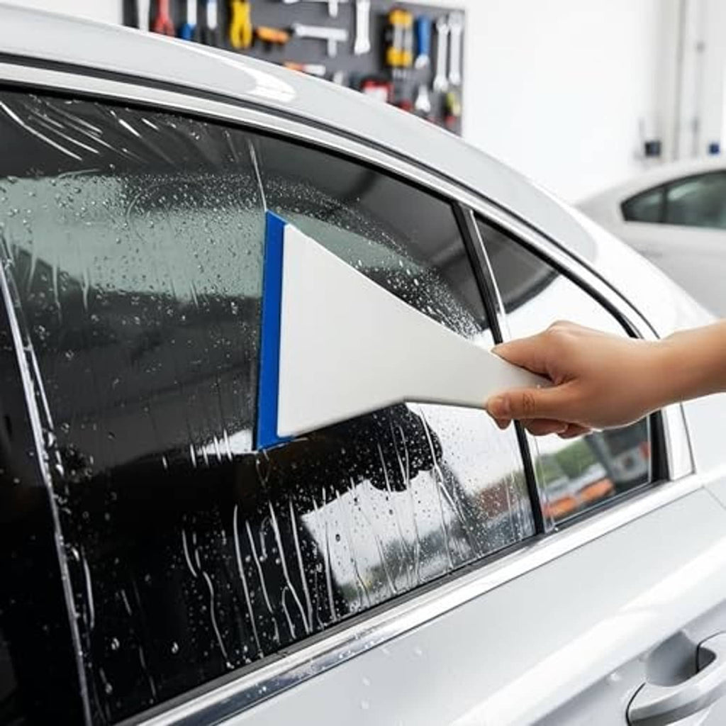 Hand applying window tint film with felt-edge squeegee on car door glass.