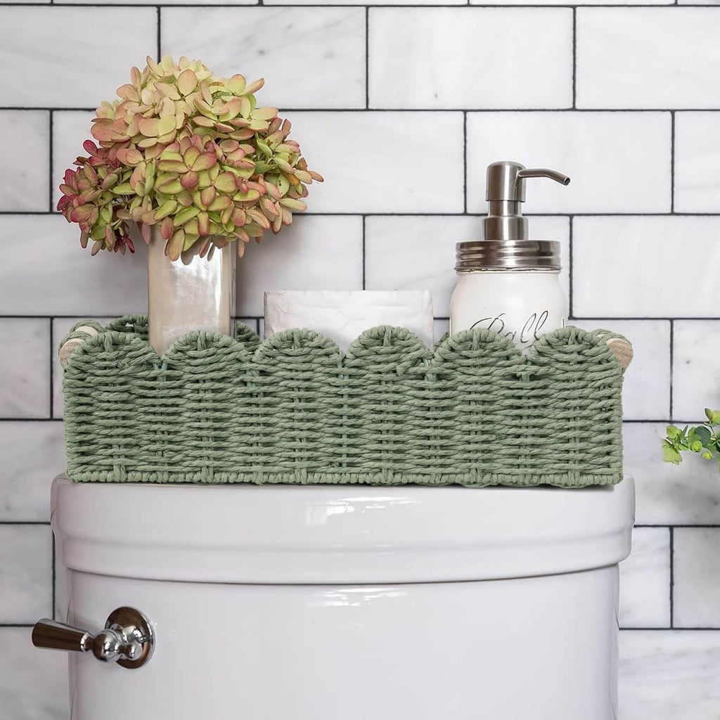 Green woven scalloped basket with wood handles on toilet tank, toiletries inside