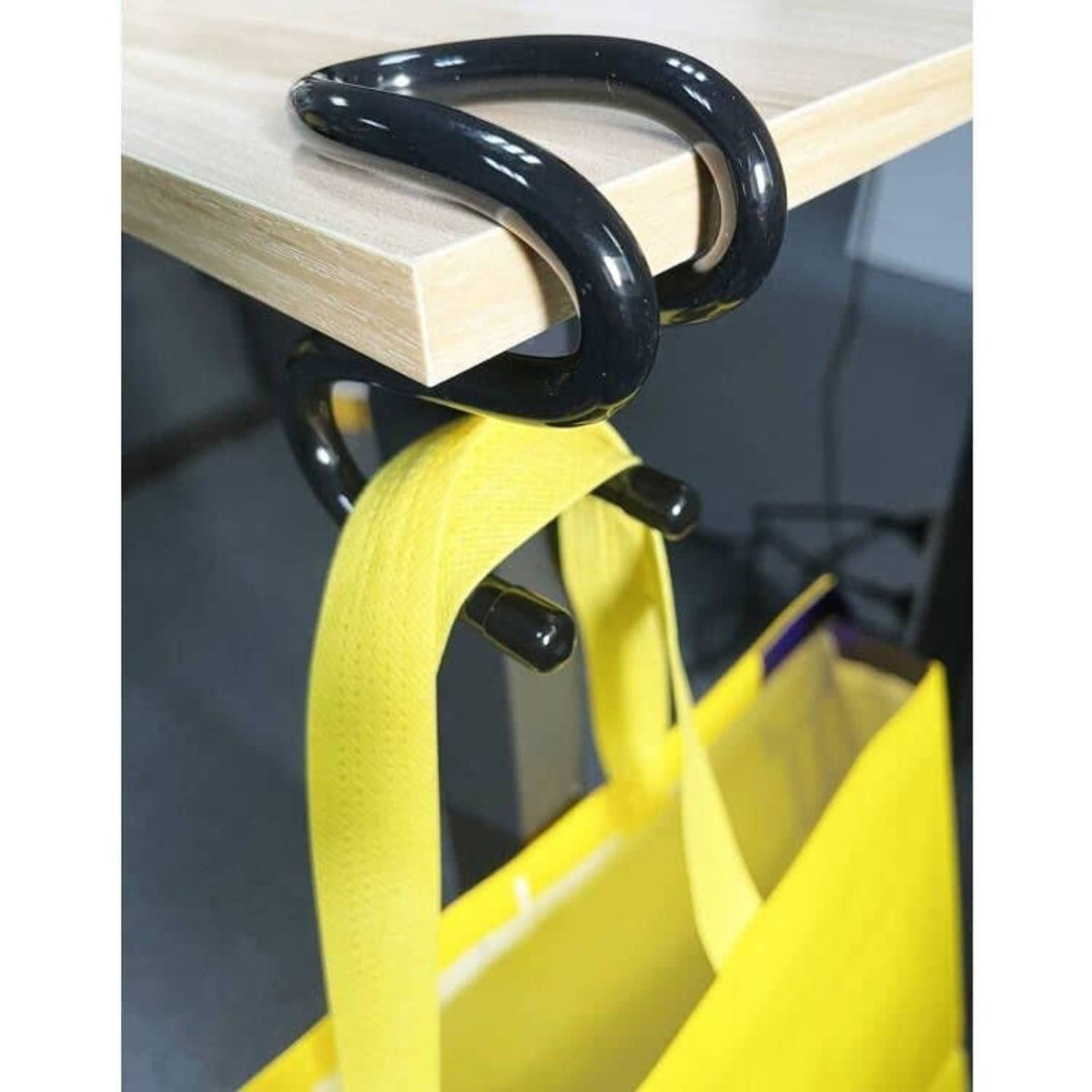 Black bag hook clamp holding a bright yellow tote bag from a wooden shelf