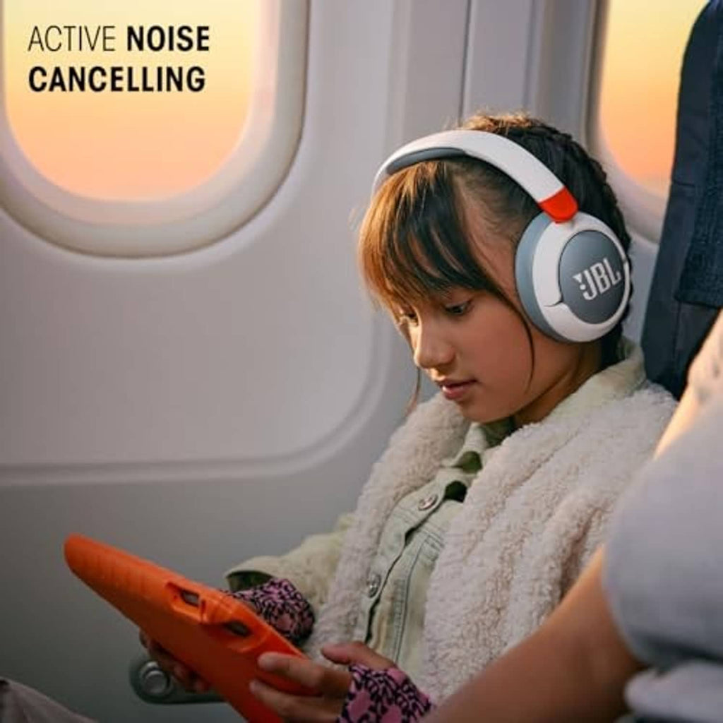 Child wearing white and gray over-ear JBL noise-cancelling headphones, orange ear tips.