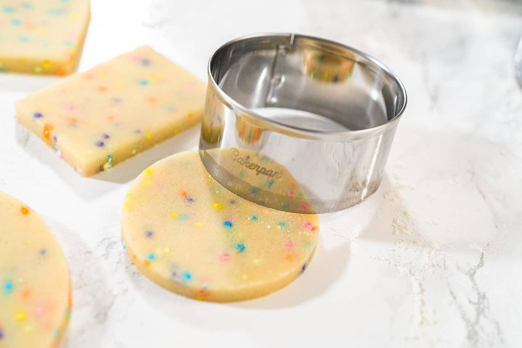 Round stainless steel cookie cutter with sprinkle cookies on the counter.