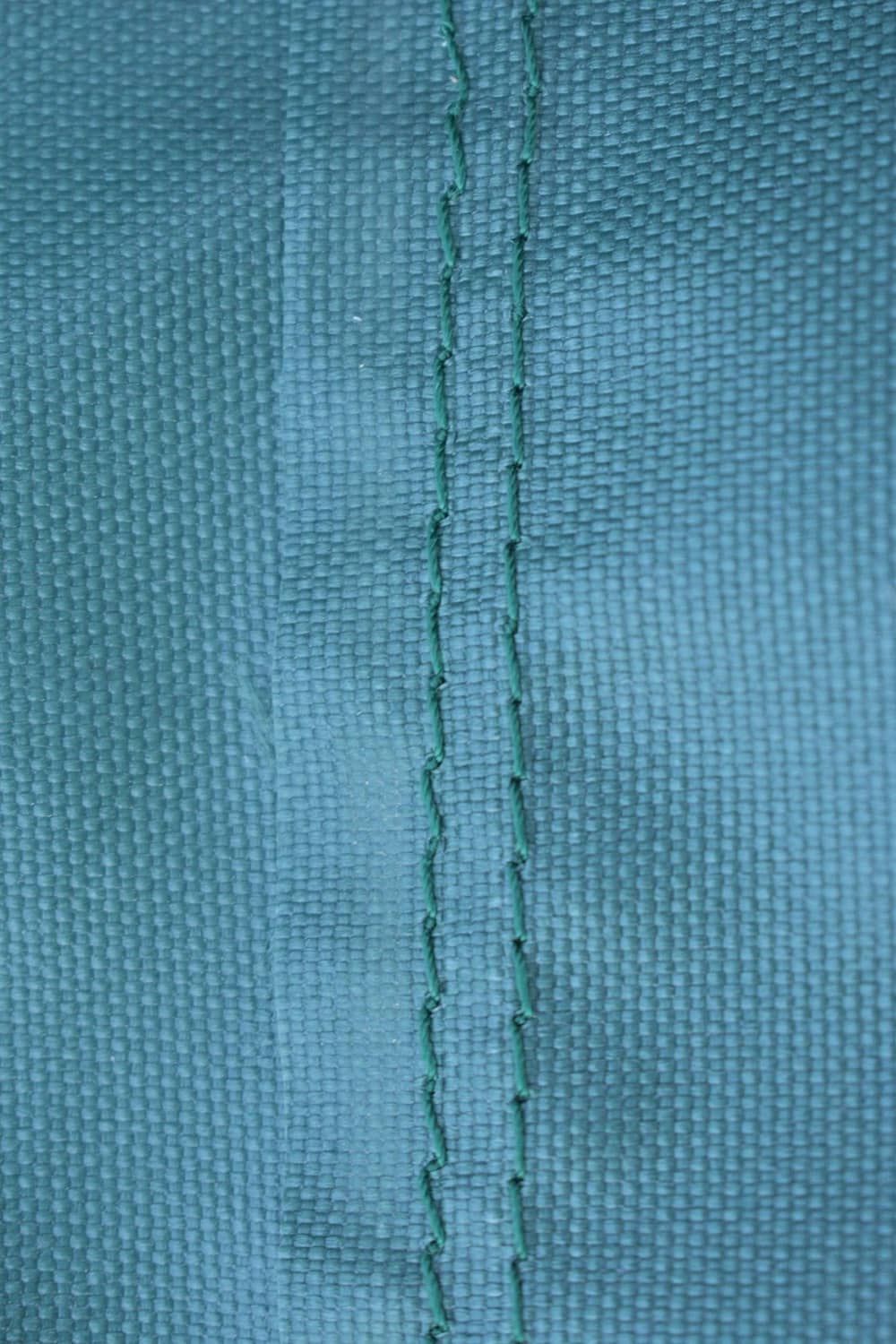 Dark teal fabric grill cover seam stitching close-up, stitched panel line visible