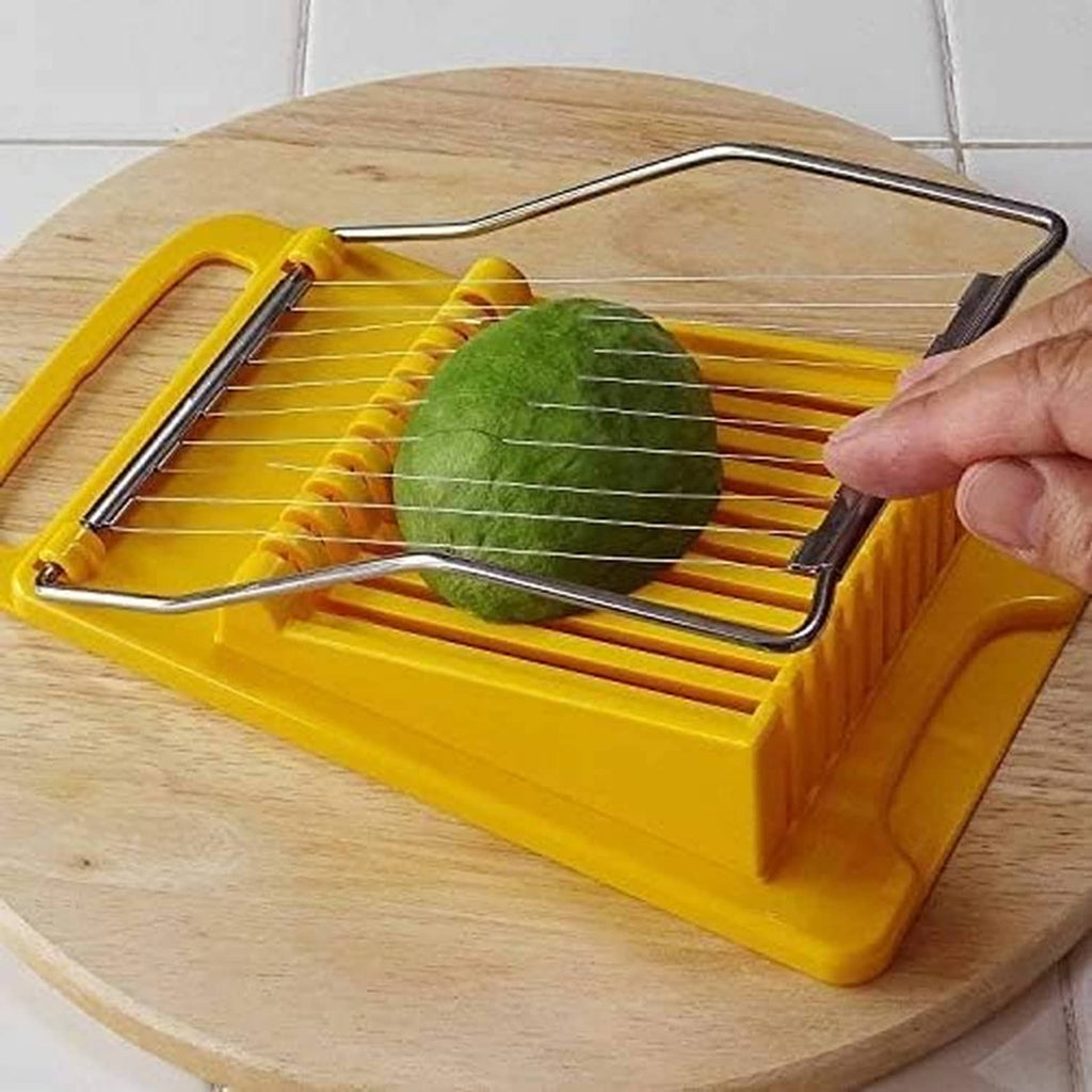 Yellow slicer tool cutting green produce with a metal wire grid on a wooden board