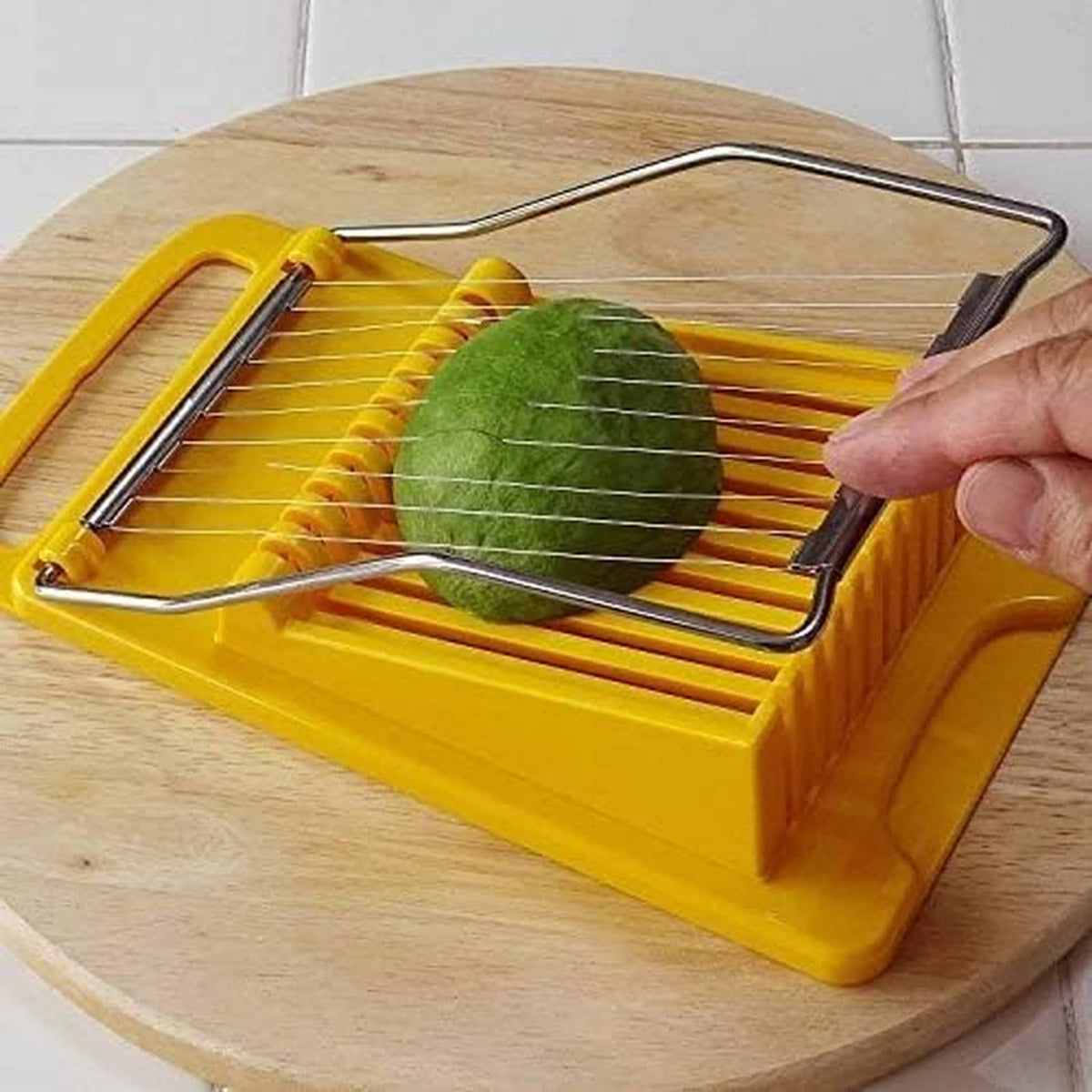 Yellow slicer tool cutting green produce with a metal wire grid on a wooden board