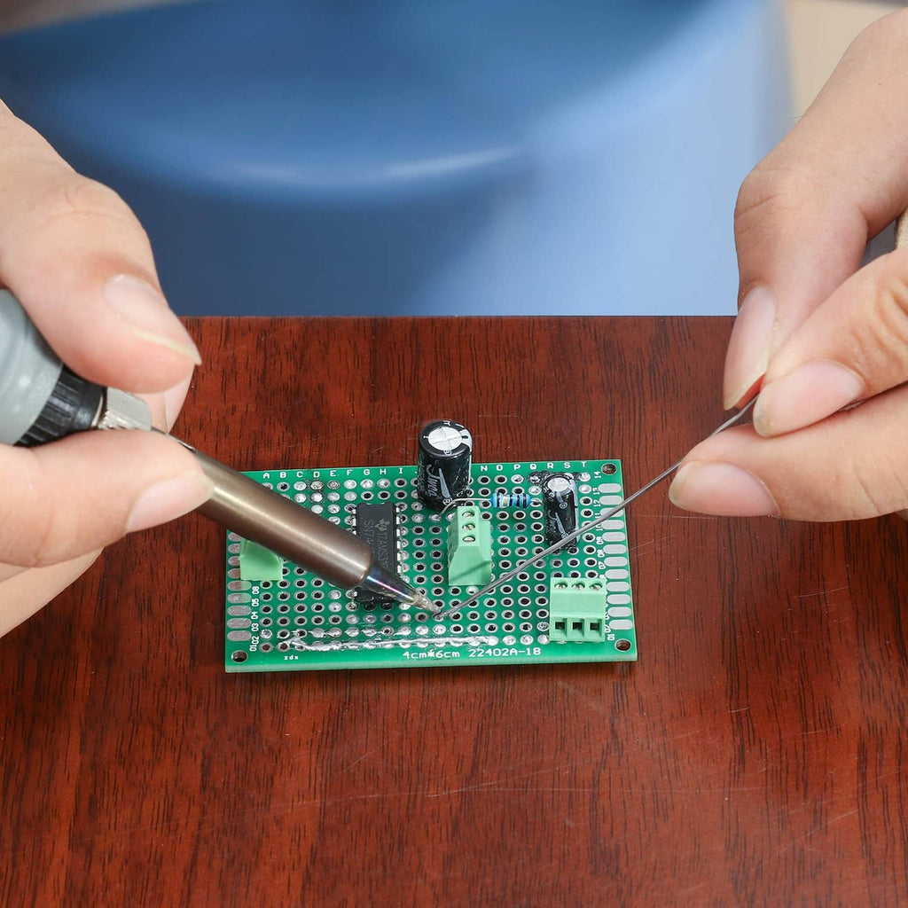 Green PCB prototyping board being soldered with a wire and soldering iron