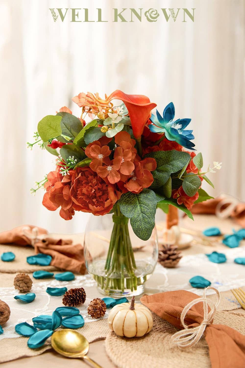 Teal and orange faux flower bouquet in clear glass vase with green leaves