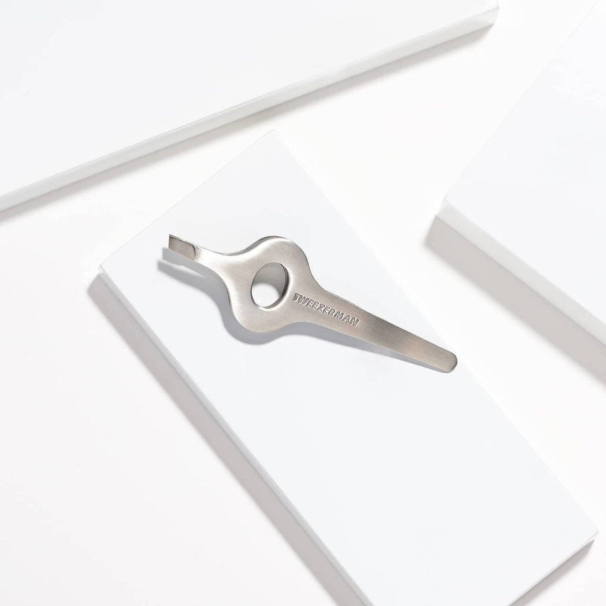 Silver wide grip slant tweezer resting on white box