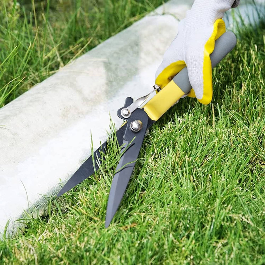 Yellow grass trimming shears with dark blades cutting along a lawn edge