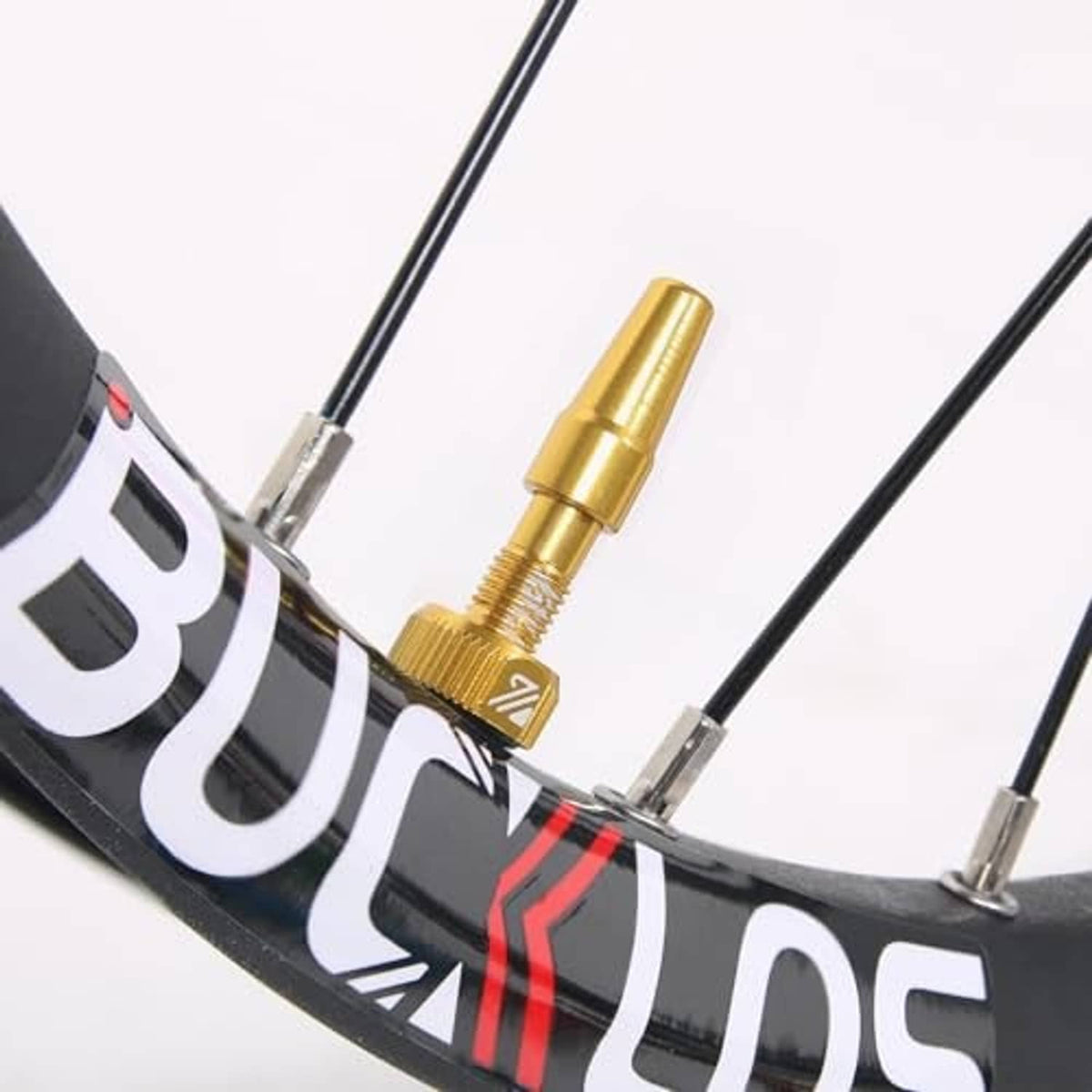 Gold Presta tubeless valve stem installed on a bicycle rim, with threaded stem and cap.