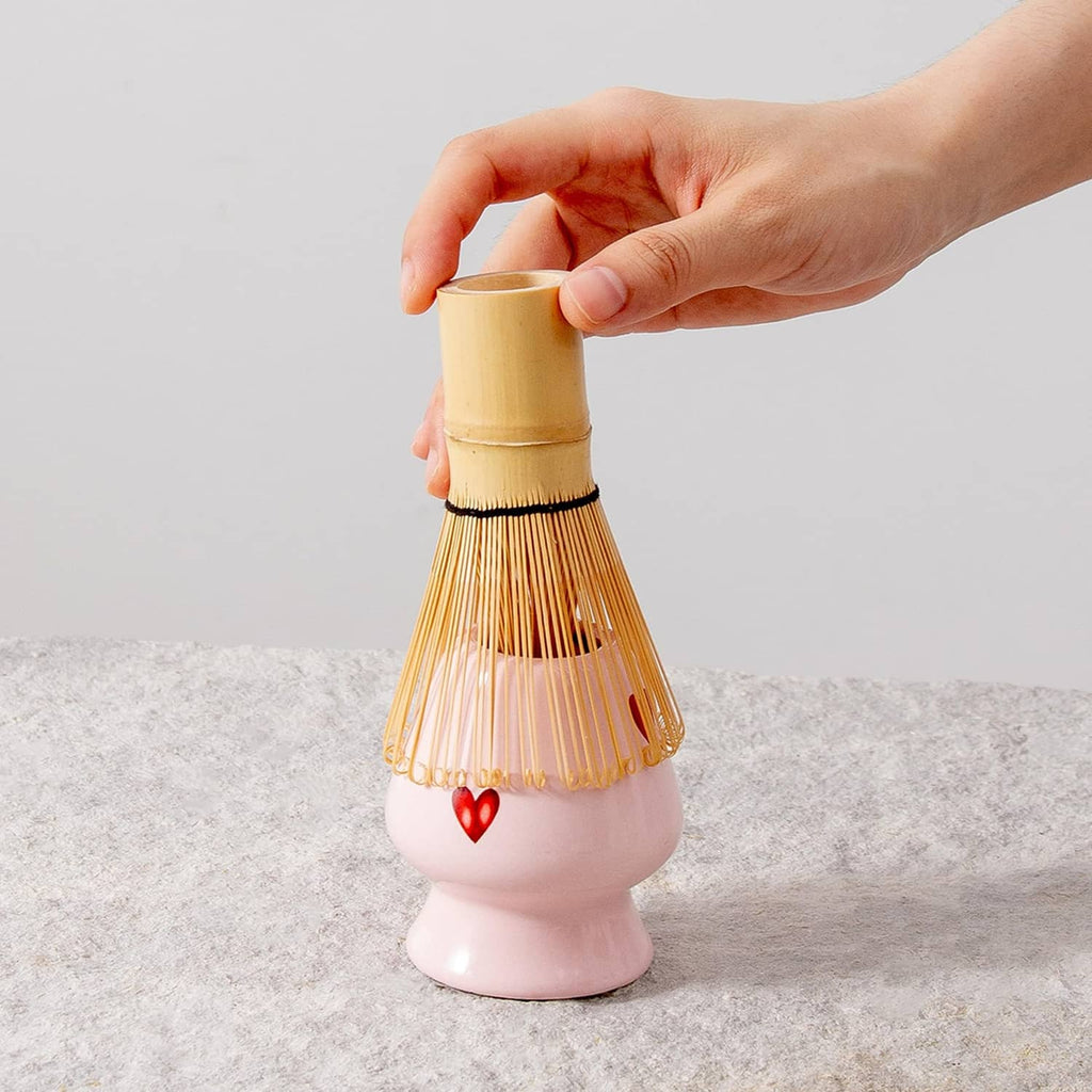 Bamboo matcha whisk held above a pink ceramic whisk holder