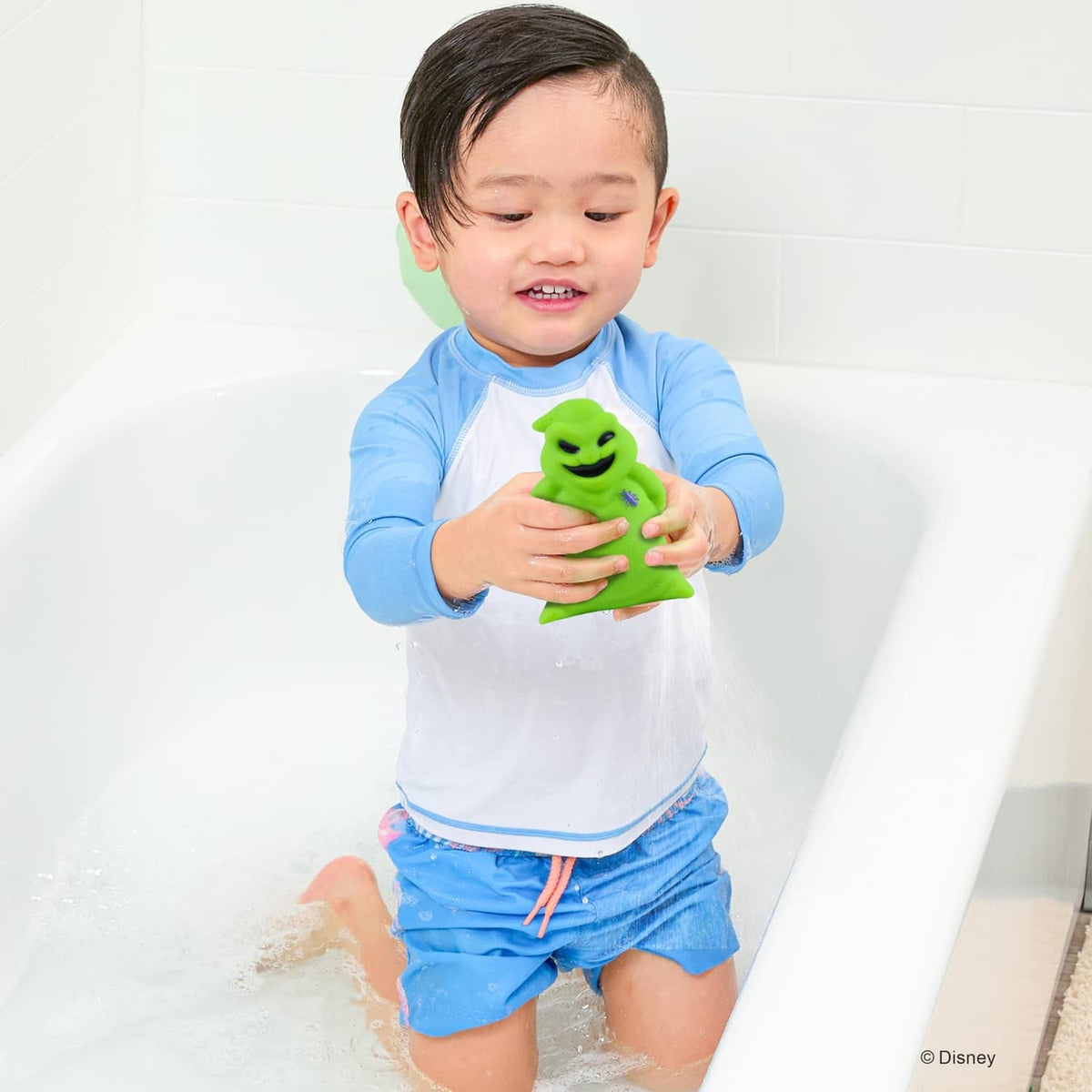 Child holding green jumbo bath squirter figure in the bathtub