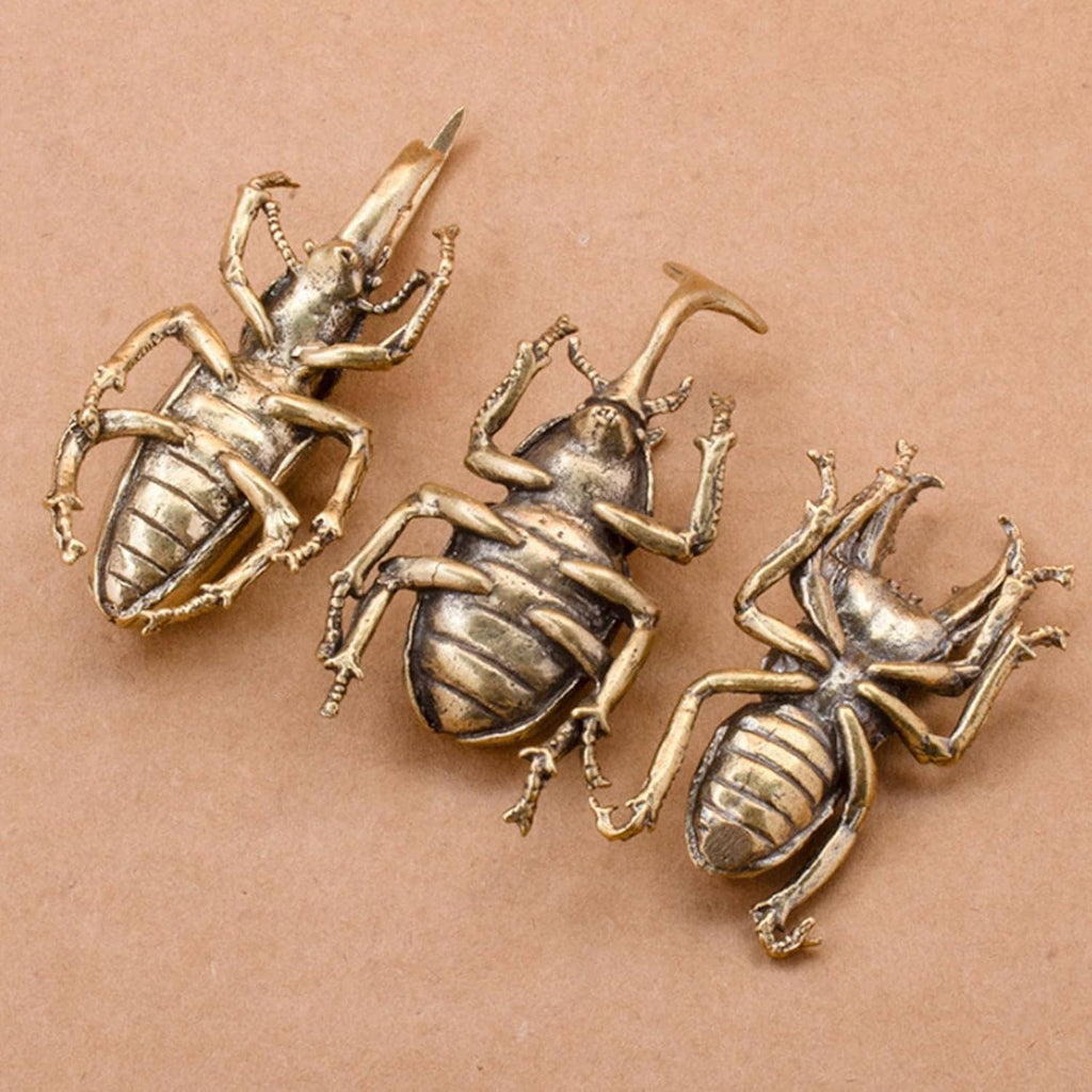 Three miniature brass beetle ornaments on a flat surface, detailed wing shells