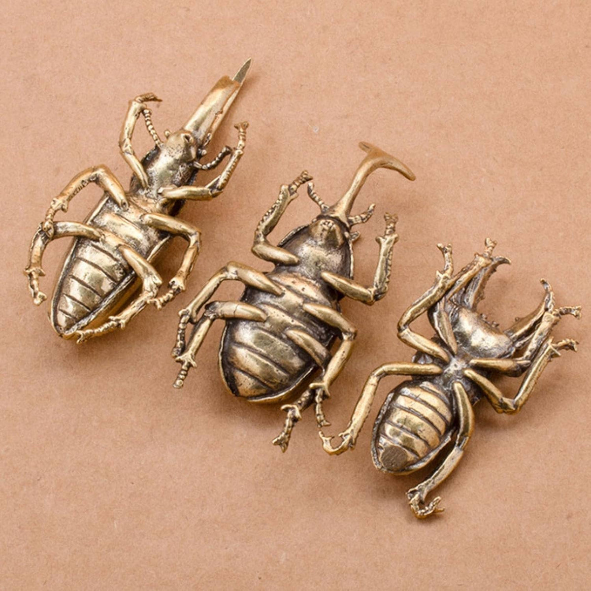 Three miniature brass beetle ornaments on a flat surface, detailed wing shells