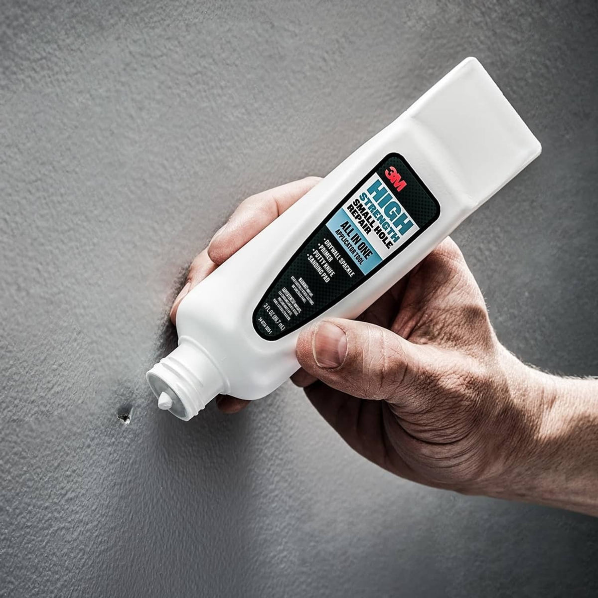 White all-in-one repair applicator tube dispensing near a small hole on textured wall